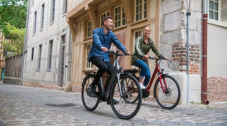 Deux personnes sur un vélo de ville en train de se déplacer sur des pavés.